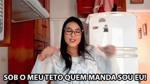 A Woman Wearing Glasses Is Standing In Front Of A Refrigerator With Sob O Meu Teto Quem Manda Sou Eu Written On It GIF