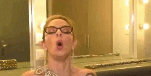 A Woman Wearing Glasses Is Taking A Selfie In Front Of A Mirror In A Room . GIF
