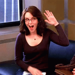 A Woman Wearing Glasses Is Waving Her Hand While Sitting On A Couch GIF