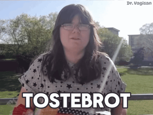 a woman wearing glasses says tostebrot in front of a grassy field