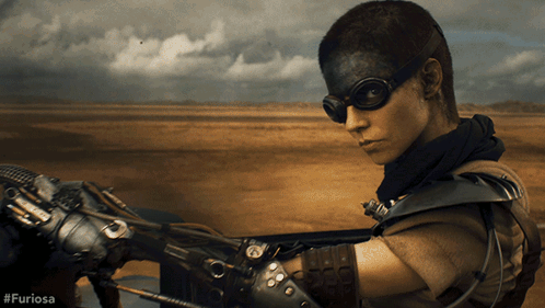A Woman Wearing Goggles And A Mask Is Riding A Motorcycle With #Furiosa Written On The Bottom GIF