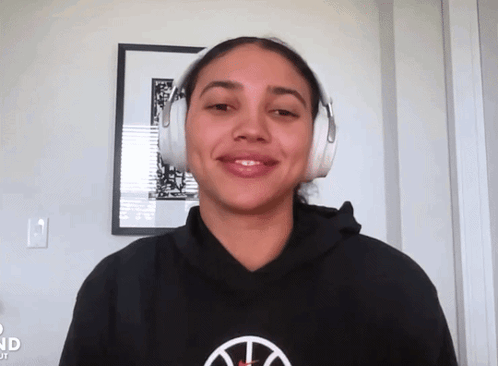A Woman Wearing Headphones And A Black Hoodie With A Basketball Logo GIF