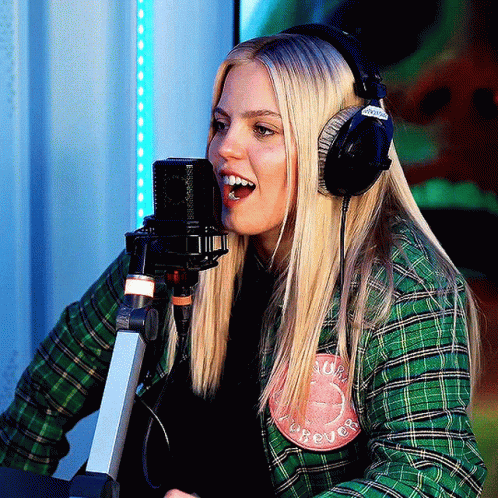 A Woman Wearing Headphones And A Green Plaid Shirt Has A Patch On Her Shirt That Says Forever GIF
