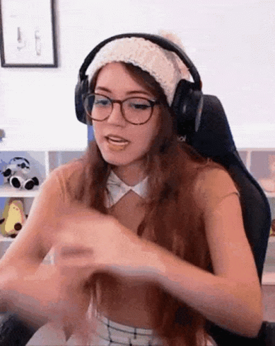 A Woman Wearing Headphones And A Hat Is Sitting In A Chair . GIF