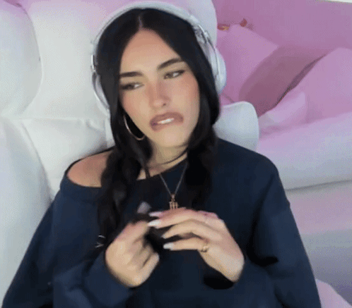 A Woman Wearing Headphones And A Necklace Is Sitting On A Pink Couch GIF