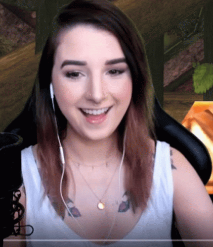 A Woman Wearing Headphones And A Necklace Smiles GIF
