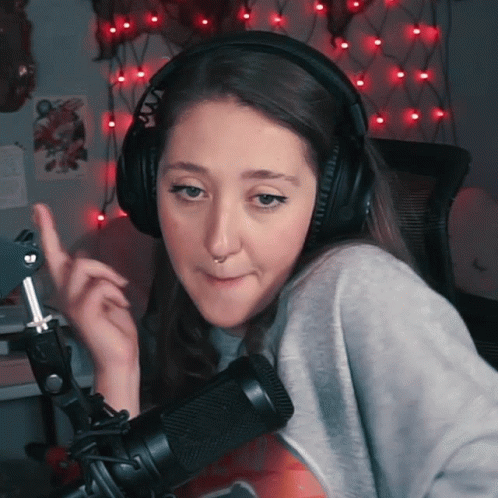 A Woman Wearing Headphones And A Nose Ring Stands In Front Of A Microphone Making A Funny Face GIF