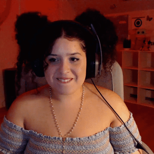 A Woman Wearing Headphones And A Pearl Necklace Is Smiling GIF