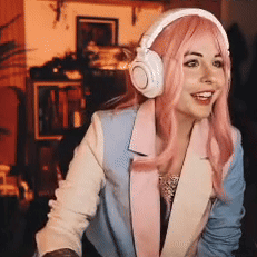 A Woman Wearing Headphones And A Pink Wig Is Smiling . GIF