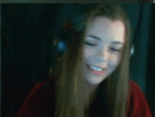 A Woman Wearing Headphones And A Red Shirt Is Smiling While Sitting In Front Of A Computer Screen . GIF