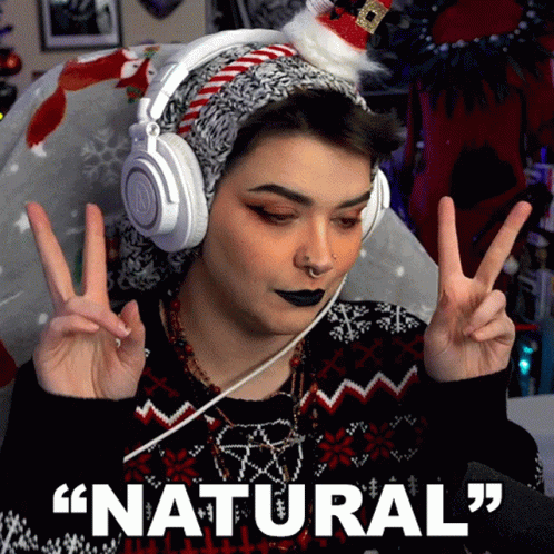 A Woman Wearing Headphones And A Santa Hat Is Giving A Peace Sign With The Words " Natural " Below Her GIF