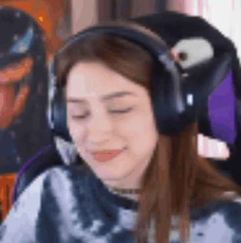 A Woman Wearing Headphones And A Tie Dye Shirt Is Sitting In A Chair With Her Eyes Closed . GIF