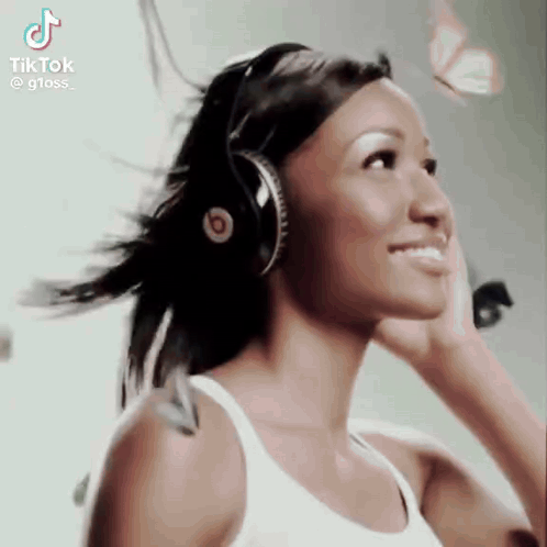 A Woman Wearing Headphones And A White Tank Top Is Smiling . GIF