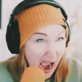 A Woman Wearing Headphones And An Orange Beanie Eating A Carrot GIF