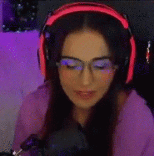A Woman Wearing Headphones And Glasses Is Playing A Video Game . GIF