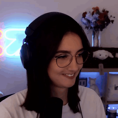 A Woman Wearing Headphones And Glasses Smiles In Front Of A Neon Sign That Says ' E2 ' GIF