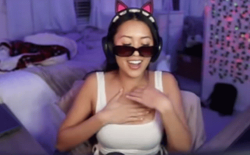 A Woman Wearing Headphones And Sunglasses Is Sitting On A Bed . GIF