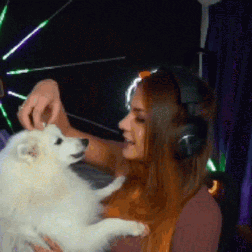 A Woman Wearing Headphones Holds A Small White Dog GIF