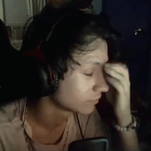 A Woman Wearing Headphones Is Crying While Sitting In Front Of A Computer Screen . GIF