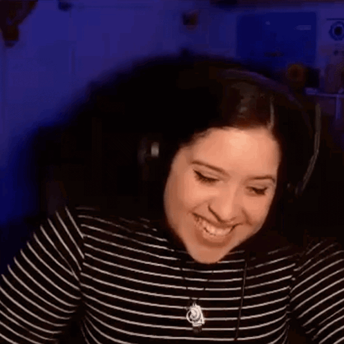 A Woman Wearing Headphones Is Laughing While Sitting In Front Of A Computer Screen . GIF
