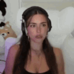 A Woman Wearing Headphones Is Sitting In A Chair And Looking At The Camera . GIF
