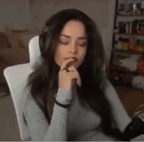 A Woman Wearing Headphones Is Sitting In A Chair With Her Eyes Closed And Her Hands On Her Chin . GIF
