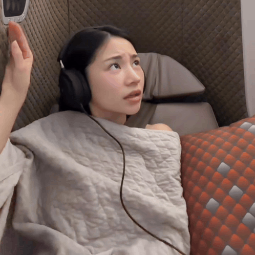 A Woman Wearing Headphones Is Sitting On A Couch With A Pillow GIF