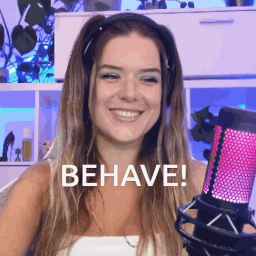 A Woman Wearing Headphones Is Smiling And Holding A Microphone With The Word Behave Written On It GIF