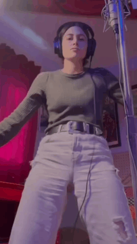 A Woman Wearing Headphones Is Standing In Front Of A Microphone . GIF