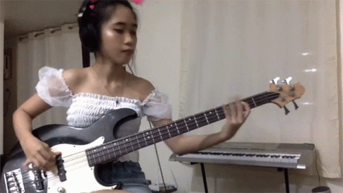 A Woman Wearing Headphones Plays A Bass Guitar GIF