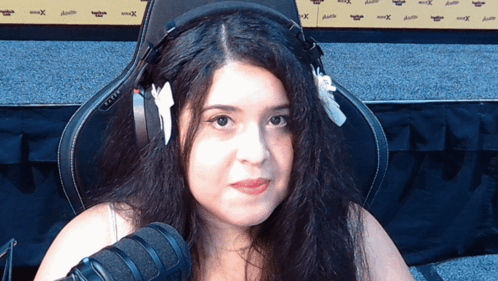 A Woman Wearing Headphones Sits In Front Of A Microphone And A Wall That Says Xtreme GIF