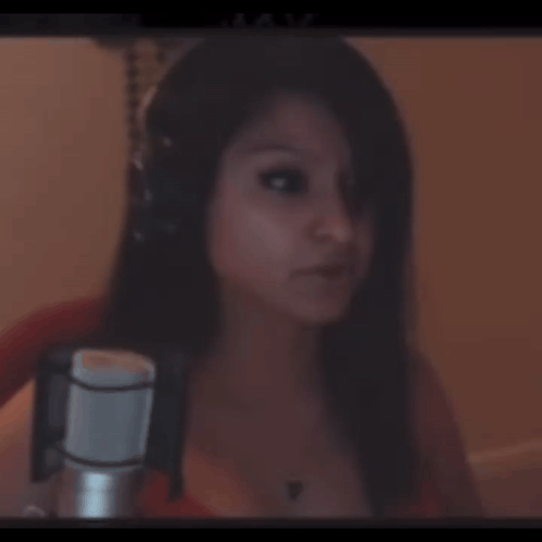 A Woman Wearing Headphones Stands In Front Of A Microphone And Looks At The Camera GIF