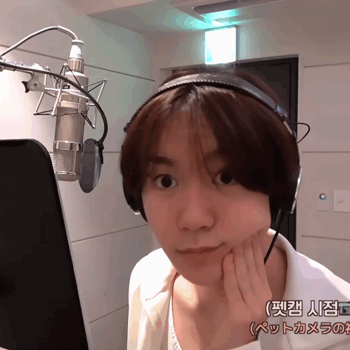 A Woman Wearing Headphones Stands In Front Of A Microphone In A Room With Chinese Writing On The Wall Behind Her GIF