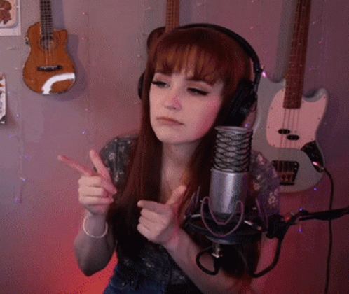 A Woman Wearing Headphones Stands In Front Of A Microphone With Guitars Behind Her GIF