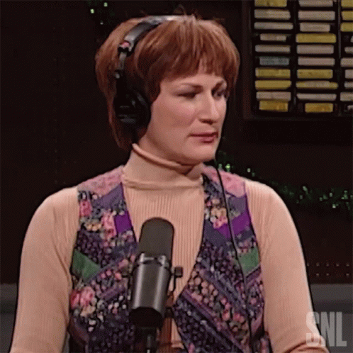 a woman wearing headphones stands in front of a microphone with the snl logo in the background