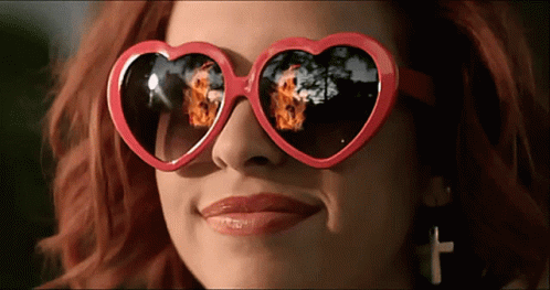 A Woman Wearing Heart Shaped Sunglasses With A Reflection Of Fire GIF