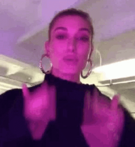 A Woman Wearing Hoop Earrings And A Black Turtleneck Is Making A Funny Face . GIF
