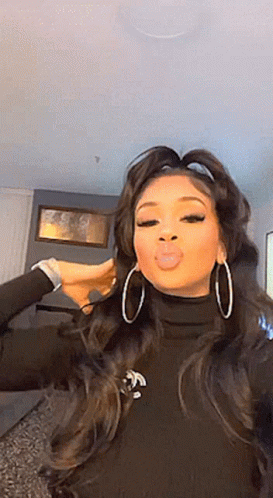 A Woman Wearing Hoop Earrings And A Black Turtleneck Is Making A Funny Face . GIF
