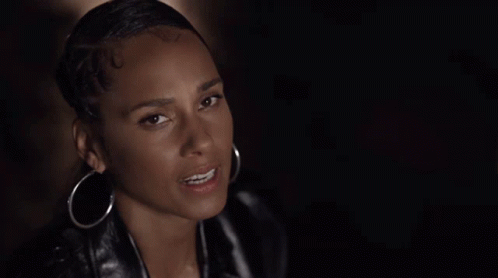A Woman Wearing Hoop Earrings And A Leather Jacket Looks At The Camera . GIF