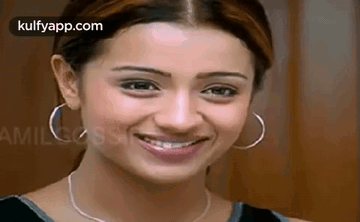 A Woman Wearing Hoop Earrings And A Necklace Is Smiling For The Camera . GIF