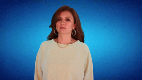A Woman Wearing Hoop Earrings And A Necklace Looks At The Camera GIF