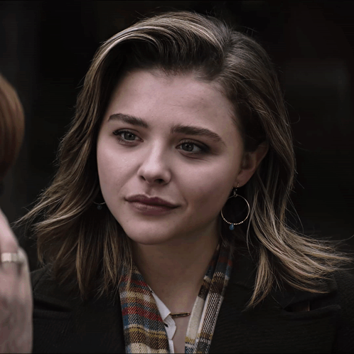 A Woman Wearing Hoop Earrings And A Plaid Scarf Looks At The Camera GIF