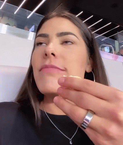 A Woman Wearing Hoop Earrings And A Silver Ring Looks At Something GIF