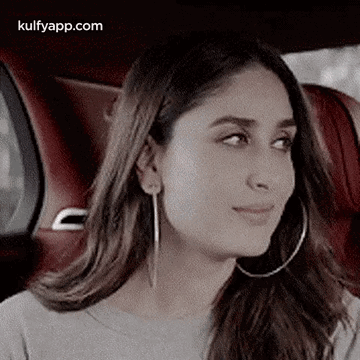 A Woman Wearing Hoop Earrings Is Sitting In A Car And Looking At The Camera . GIF