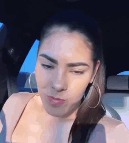 A Woman Wearing Hoop Earrings Is Sitting In A Car And Making A Funny Face GIF