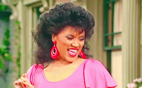 A Woman Wearing Red Earrings And A Pink Shirt Is Smiling GIF
