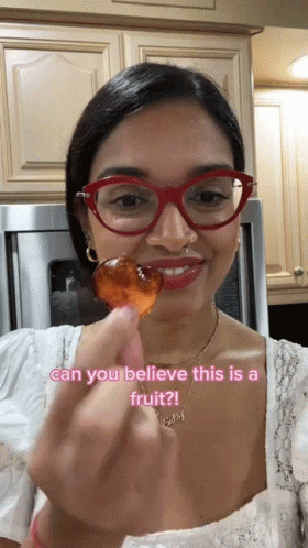 A Woman Wearing Red Glasses Is Holding A Piece Of Fruit With The Caption Can You Believe This Is A Fruit ? GIF