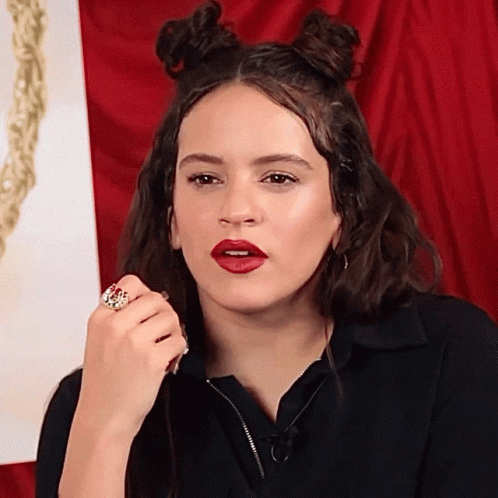 A Woman Wearing Red Lipstick And A Ring On Her Finger Looks At The Camera GIF