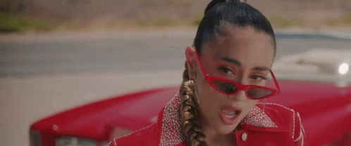 A Woman Wearing Red Sunglasses And A Red Jacket Is Standing Next To A Red Car . GIF