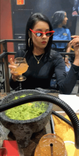 A Woman Wearing Red Sunglasses Sits At A Table With A Bowl Of Guacamole On It GIF
